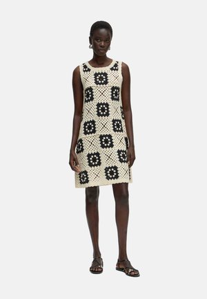 Kurzes Kleid aus einem Häkelstoff mit einem beigen Grundton und schwarzen Blumenmustern im Rautendesign. Ärmellos mit rundem Ausschnitt.