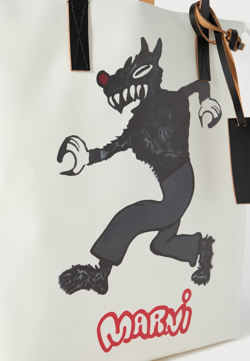 Sac fourre-tout blanc avec un personnage de loup noir ayant un nez rouge, portant un pantalon noir. Logo "Marni" en rouge en bas. Anses en cuir noir.
