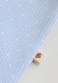 Tissu côtelé bleu clair avec de petits pois blancs et une étiquette en tricot crème présentant un motif de fraise rouge et verte.