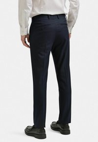 Marinblå skräddarsydda byxor i texturerad tyg, med platta fickor som har knappstängning. Bärs med en vit skjorta och svarta loafers.