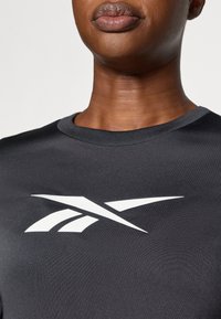 Melns sportisks T-krekls ar noapaļotu kakla izgriezumu un īsām piedurknēm, uz kuras krūtīm ir izteikts balts logotips. Mīksts, gluds audums.