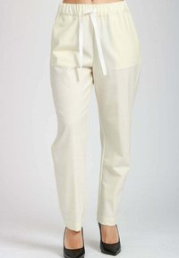 Pantaloni dritti color crema con vita elasticizzata e cordoncino bianco, indossati con décolleté nere a punta.