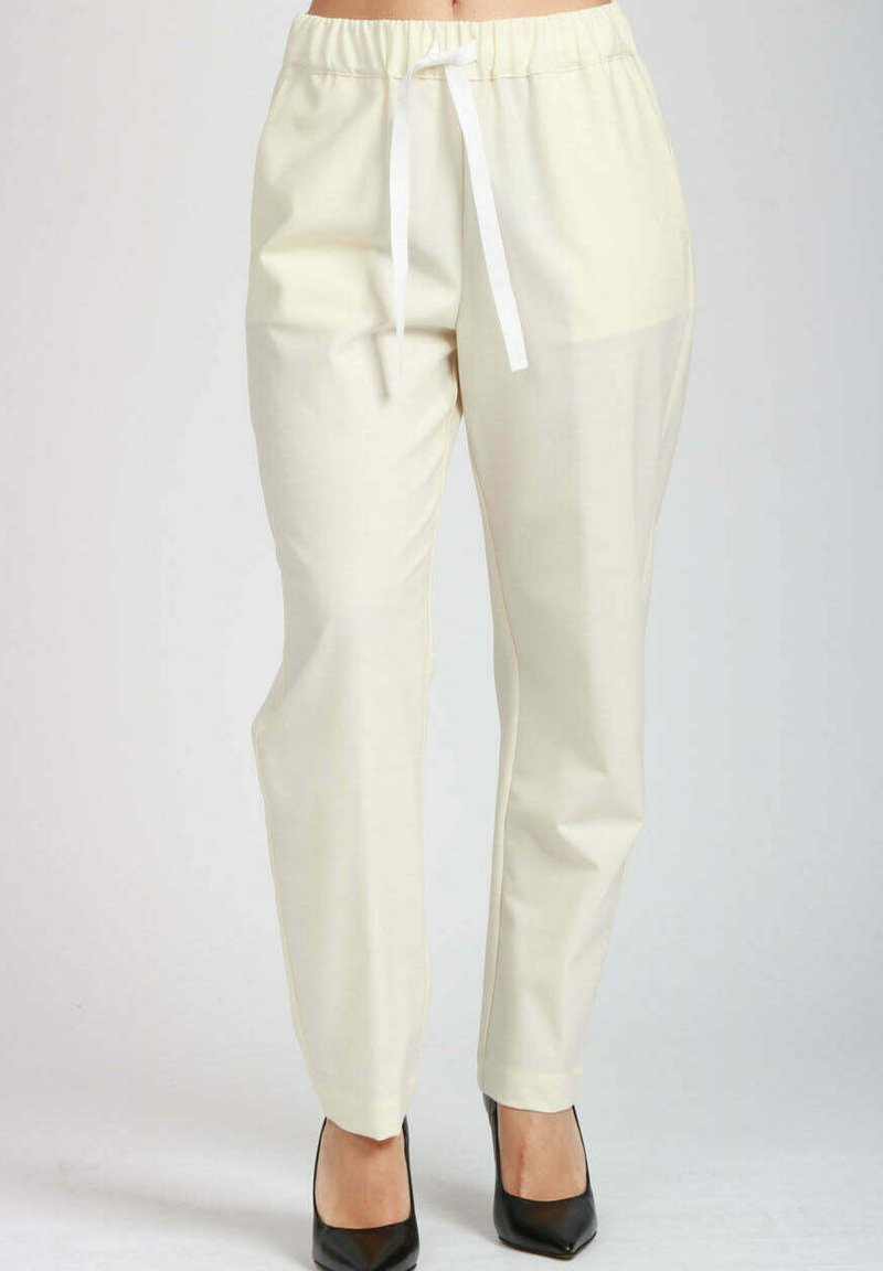 Pantaloni dritti color crema con vita elasticizzata e cordoncino bianco, indossati con décolleté nere a punta.