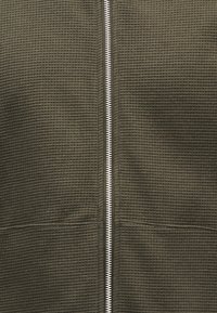 Φυστικί μπουφάν με φερμουάρ και υφή βάφλας, με ασημένιο φερμουάρ και δύο μπροστινές τσέπες στα πλαϊνά.