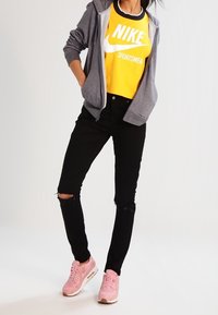 Grå zip-up hoodie, gul Nike sport t-shirt, svarta rivna jeans och rosa Nike sneakers. Fokusera på sportigt avslappnad stil.