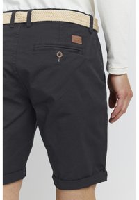 Shorts noirs en coton au toucher lisse, avec ourlets roulés, une poche arrière avec un bouton et une ceinture tissée beige.