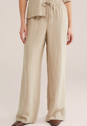 Beżowe szerokie spodnie z elastycznym pasem i sznurkiem, noszone z dopasowanym topem i brązowymi zakostkowanymi butami.