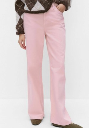 Femme portant un pantalon droit rose clair avec un pull marron et blanc à motif losange, debout avec une main dans la poche.