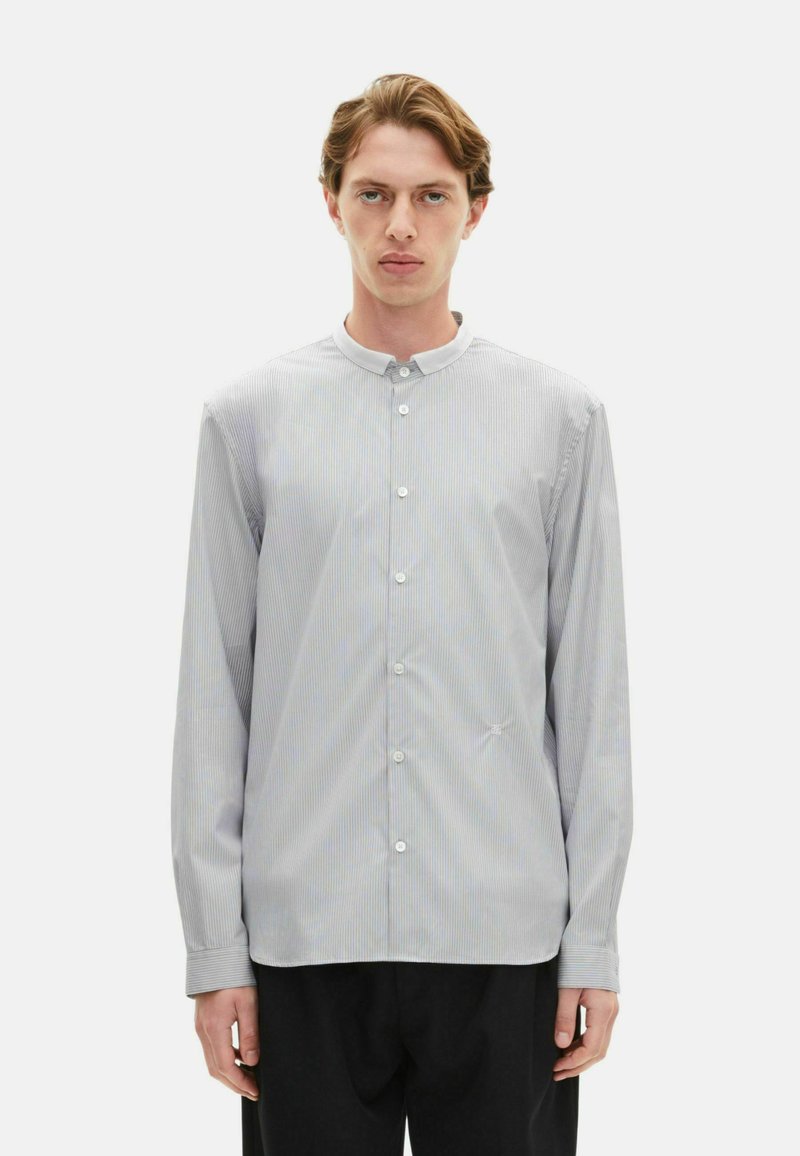 Koszula zapinana na guziki w jasnoniebieskie i białe pionowe paski, z okrągłym kołnierzykiem, długimi rękawami i subtelnym haftem na dolnym brzegu.