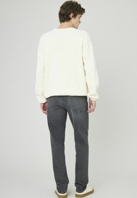 Pull en maille blanche à épaules tombantes, associé à un jean gris slim avec deux poches arrière, porté avec des baskets beiges.