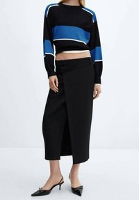 Zwarte lange rok met een zijsplit, gecombineerd met een cropped zwart sweater met blauw en witte horizontale strepen. Zwarte puntige hakken.