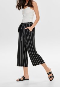Zwart-witte gestreepte cropped broeken met een strik in de taille, gecombineerd met zwarte platte sandalen met studs.