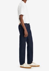 Mörkblå denimjeans med rak ben, i kombination med en enkel vit t-shirt med kort ärm och vita sneakers med gummisula.