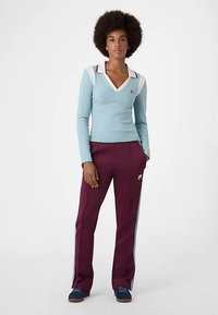 Maglione azzurro chiaro a scollo a v con dettagli bianchi e bordeaux, abbinato a pantaloni bordeaux con strisce laterali azzurre e dettaglio logo. Scarpe blu.