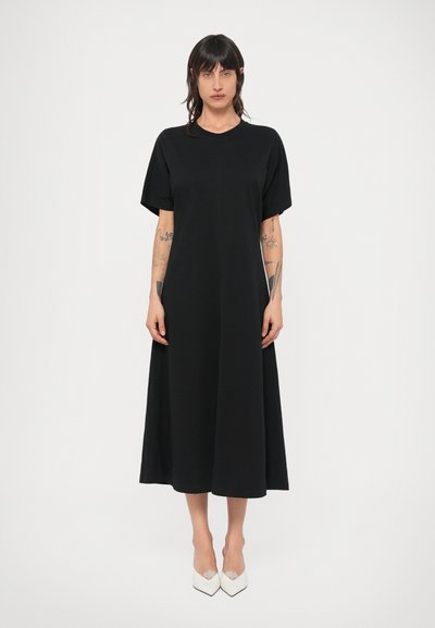Robe noire jusqu'aux genoux avec manches courtes, encolure ronde et silhouette décontractée. Assortie à des chaussures blanches à bouts pointus.