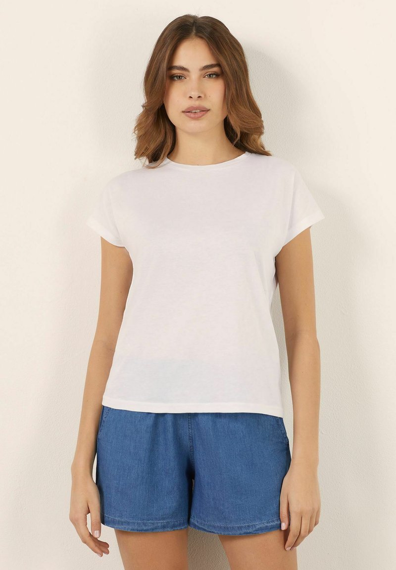 Weißes T-Shirt mit kurzen Ärmeln aus leichtem Stoff, mit rundem Ausschnitt und lässigem Schnitt. Kombiniert mit Jeansshorts.