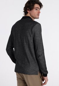 Langarm-Polohemd in Dunkelgrau, mit schwarzem Kragen, strukturiertem Stoff und seitlichen Schlitzen für mehr Bewegungsfreiheit.