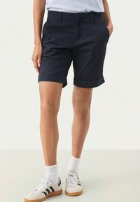 Marina bomullsshorts med upprullade fållar, framfickor och en slät design, kombinerat med vita sneakers och strumpor som når till vaden.