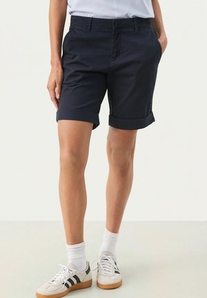 Pantalones cortos de algodón en color navy con puños enrollados, bolsillos delanteros y un diseño de frente plano, combinados con zapatillas blancas y calcetines de longitud de tripulación.