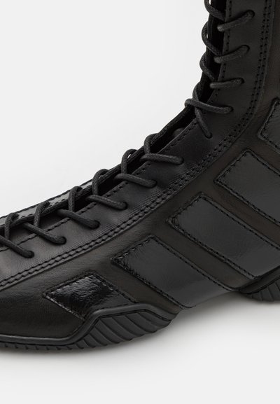 Botte noire à lacets fabriquée en cuir lisse avec des accents texturés noirs et une semelle en caoutchouc striée. Comprend des détails cousus et un motif de logo.