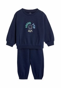 Granatowy zestaw bluzy i spodni dresowych, z okrągłym dekoltem, ściągaczami przy mankietach oraz haftowanym napisem "SUPER FUN DAY" z uśmiechniętą buźką. Miękka tekstura materiału.
