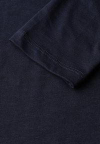 Tissu côtelé bleu marine avec une texture lisse. L'image montre un gros plan de l'ourlet et du bord de la manche, mettant en avant des détails de couture soignés.