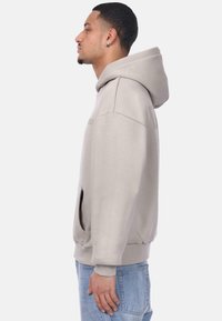 Bežna pamučna dukserica s velikom kapuljačom, prednjim džepom i rebrastim manžetama. Blago oversized kroj, s minimalnim detaljima dizajna.