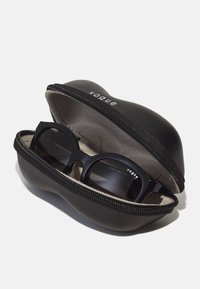 Ochelari de soare negri într-un etui tare cu fermoar. Etuiul are un exterior neted, în timp ce interiorul are o căptușeală moale. Îmbogățit cu branding "vogue".