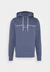 Felpa blu con coulisse bianca, tasca frontale e testo "Tommy Hilfiger Est. 1985" con logo del marchio sul petto.