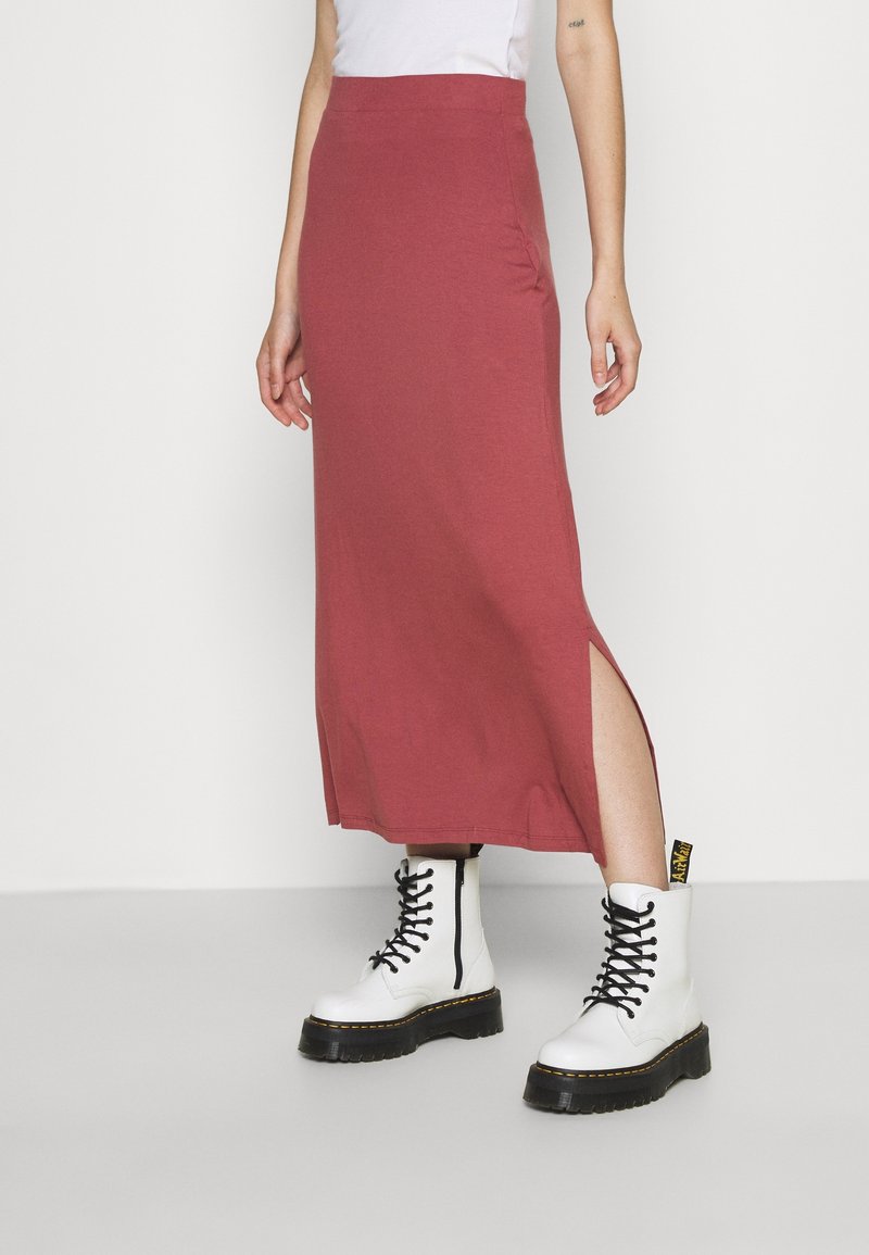 Jupe maxi en tissu mauve avec détail d'ouverture sur le côté, associée à des bottes de combat blanches à lacets avec semelles noires et accents jaunes.