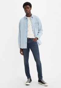 Svijetloplava traper košulja preko bijele majice i tamnoplave traperice, uparen s crnim tenisicama visokog gazišta, modernog kroja, s kopčanjem na gumbe.