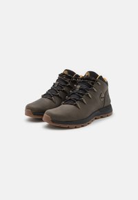 Zapatos de senderismo en cuero gris oscuro con un cuello de malla negra, con cordones negros, suelas de goma marrón y ojales de metal.