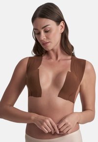 Reggiseno adesivo marrone con design a scollatura profonda, bordi senza cuciture e texture morbida. Presenta spalline per supporto e copertura.