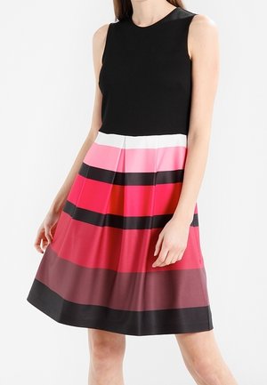 Mouwloze jurk met strak zwart bovenstuk en plissé rok met horizontale strepen in wit, roze, rood, bordeaux en zwart.
