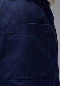 Mørkeblå bomulds shorts har en synlig baglomme med forstærket syning. Stoffet har en glat tekstur og en afslappet pasform.