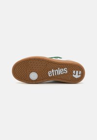 Podplat skate čevlja Etnies iz gume z grobo teksturo, z belim logotipom in okroglo blažilno komponento na sredini.
