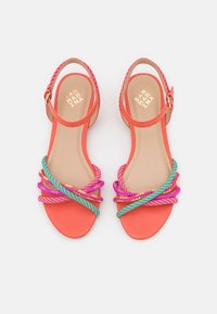 Korálové sandály s několika copánkovými pásky v růžové, fialové a tyrkysové barvě; páskem kolem kotníku zajištěné zlatou přezkou. Hladká podrážka.