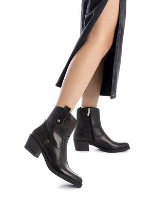 Botines de cuero negro con un tacón bajo y cuadrado, cremallera lateral y detalles de costura en contraste. Los botines tienen una punta redondeada y textura suave.