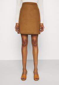 Falda mini de lana marrón con una textura suave, que presenta una cintura alta y líneas limpias. Combinada con sandalias abiertas de punta en color beige.