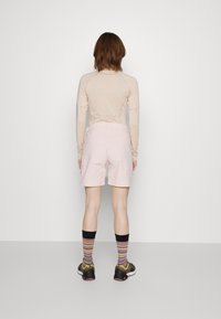 Světlé růžové šortky z měkké látky, v kombinaci s béžovým dlouhým tričkem. Vzhled doplňují pruhované podkolenky a černé sportovní boty.