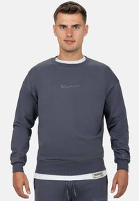 Grijze katoenen sweatshirt met ribbelstructuur, ronde halslijn en geborduurd logo. Heeft een gelaagd effect met een witte ondershirt.