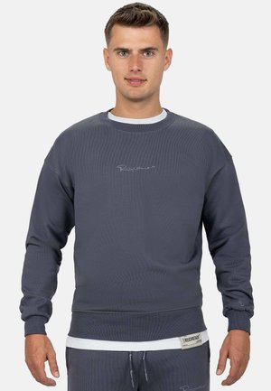 Sweatshirt en coton gris avec texture côtelée, col rond et logo brodé. Présente un effet de superposition avec un sous-vêtement blanc.