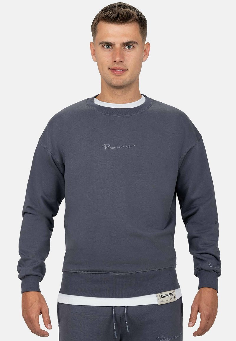 Grijze katoenen sweatshirt met ribbelstructuur, ronde halslijn en geborduurd logo. Heeft een gelaagd effect met een witte ondershirt.