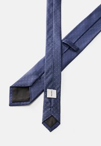 Tamsiai mėlyna kaklaraištis su mažais baltais taškeliais, pagamintas iš lygaus audinio. Turi smailų galą ir etikete su prekės ženklu Calvin Klein.