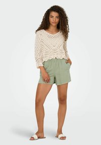 Roomkleurige gehaakte blouse met een golvende zoom en driekwart mouwen, gecombineerd met lichtgroene linnen shorts met een elastische tailleband.