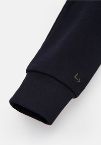 Námořnická bavlněná košile s dlouhým rukávem, rukávy s ribbovaným manžetou a malým zeleným logem, která se vyznačuje hladkou texturou a přiléhavým designem.