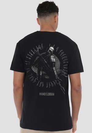 Person wearing black t-shirt with graphic of Mandalorian holding a rifle, surrounded by stylized text on the back.