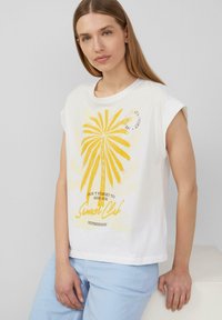 Witte katoenen T-shirt met korte mouwen, voorzien van een gele palmboomgrafiek en tekst eronder, tegen een lichte achtergrond.
