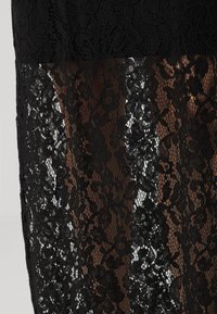 Μαύρο φόρεμα δαντέλας με σχέδιο λουλουδιών και διαφανούς και αδιαφανούς τμημάτων. Η υφή του υφάσματος έρχεται σε αντίθεση με τη λεία από κάτω στρώση.