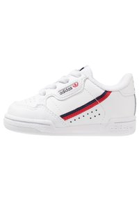 Vit idrottssko i strukturerad läder med röda och marinblå ränder, perforerade detaljer och gummisula. Logotyp på tungan och sidan.